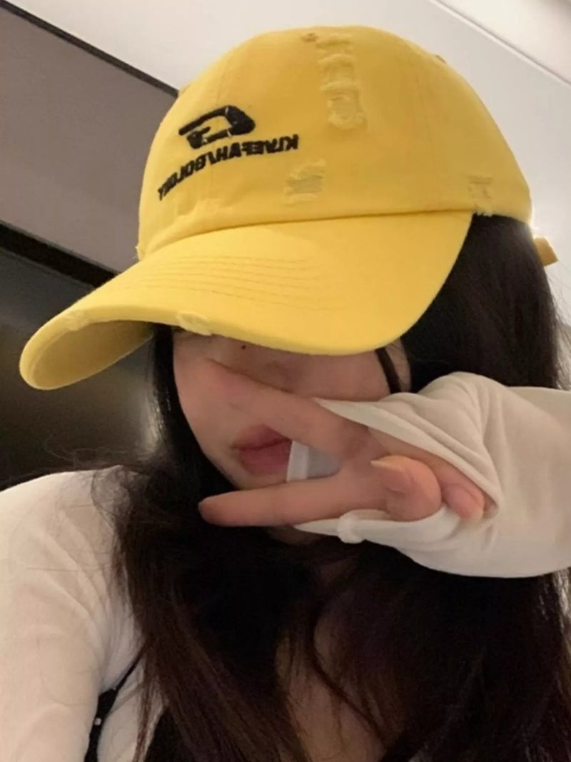 Person wearing a yellow cap with branding, making a peace sign.