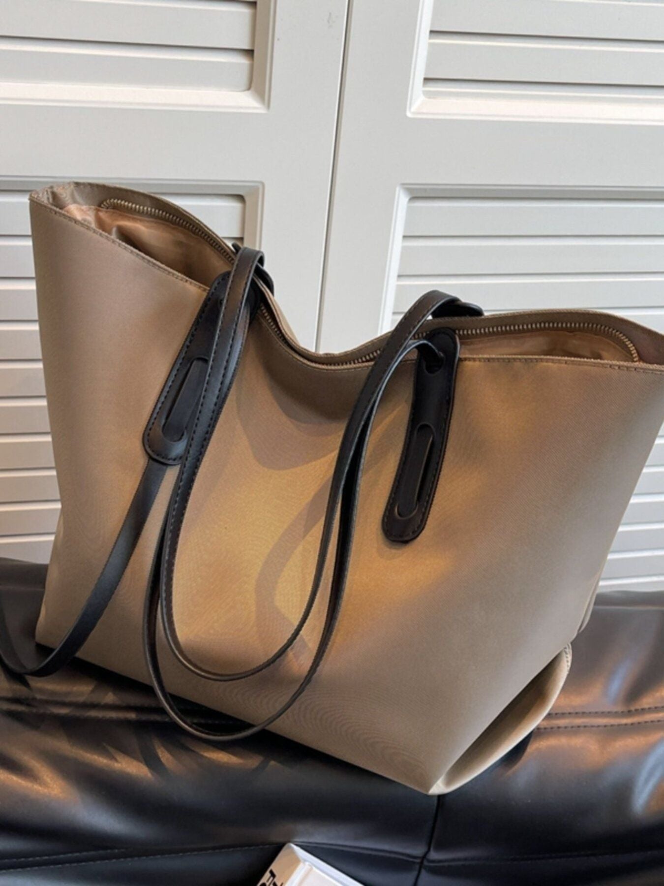 Beige handbag with black straps on a leather surface with a white background