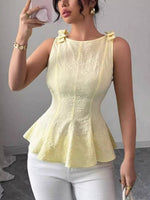 Woman wearing a yellow peplum top and white pants, taking a mirror selfie.
