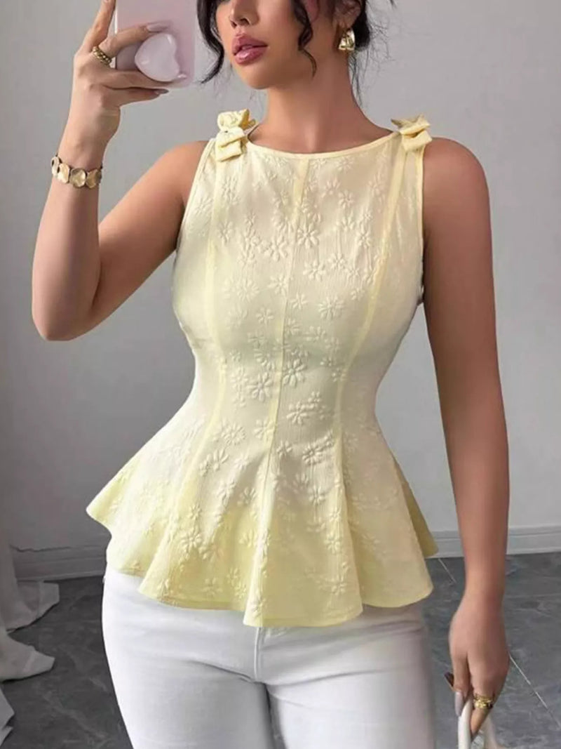 Woman wearing a yellow peplum top and white pants, taking a mirror selfie.
