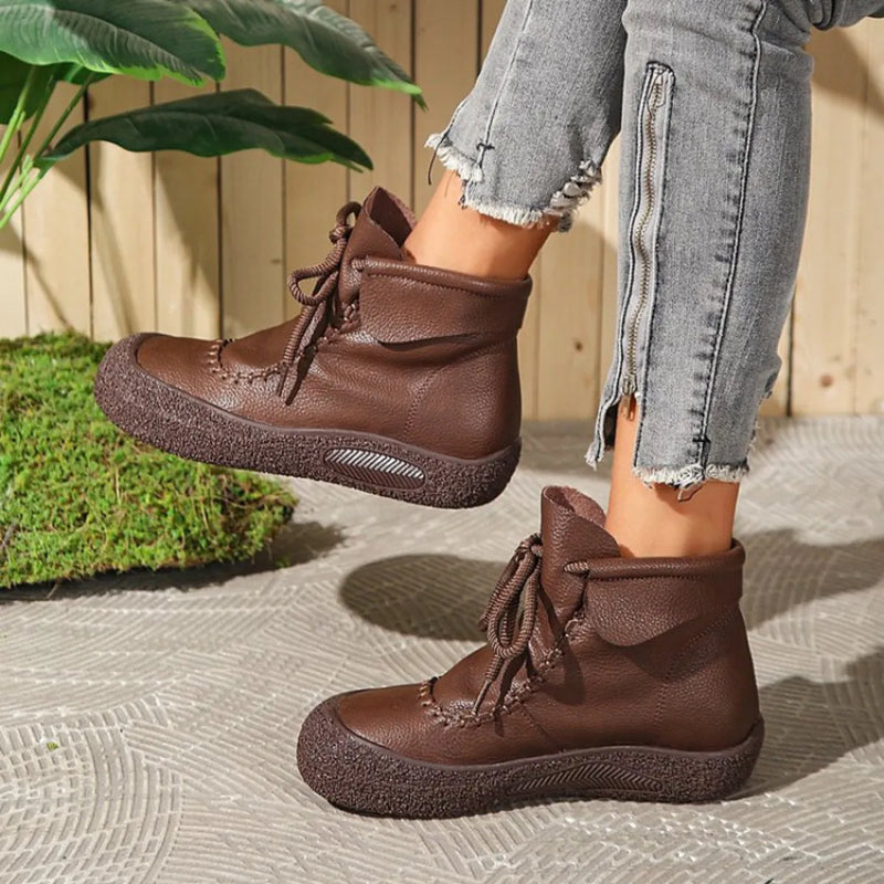 Brown boots worn with light blue jeans on a textured surface with plants in the background