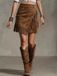 Person wearing a brown suede skirt with fringe and matching boots on a plain background