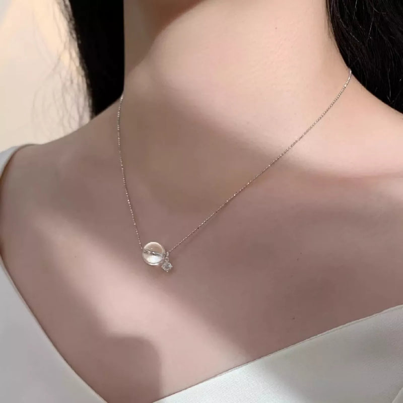 Necklace with a clear pendant on a person wearing a white top.