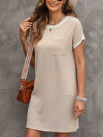 Woman wearing a beige dress with a brown leather bag against a gray background
