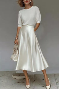 Woman wearing a white top and satin skirt with a neutral background