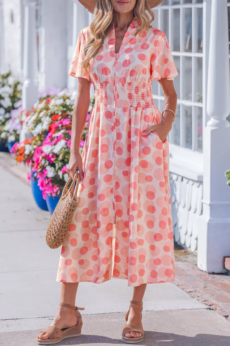 Woman wearing a pink polka dot dress with a straw bag on a sunny day.