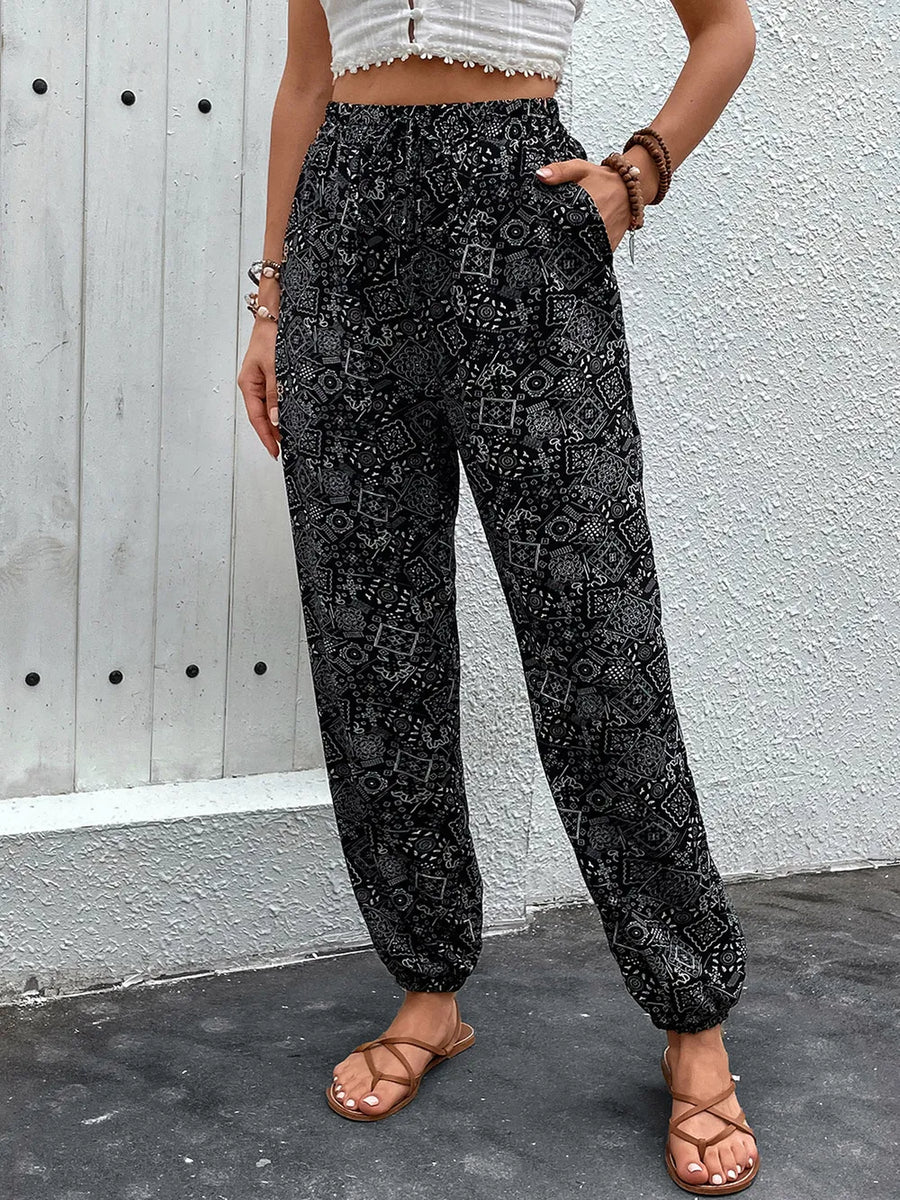 Person wearing black patterned pants against a gray wall.