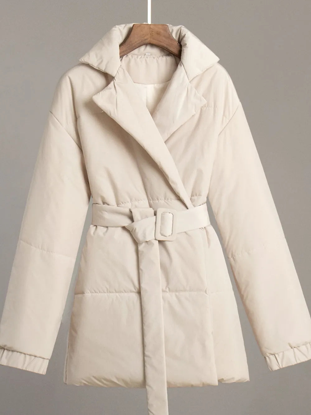 Beige puffer coat on a hanger against a gray background