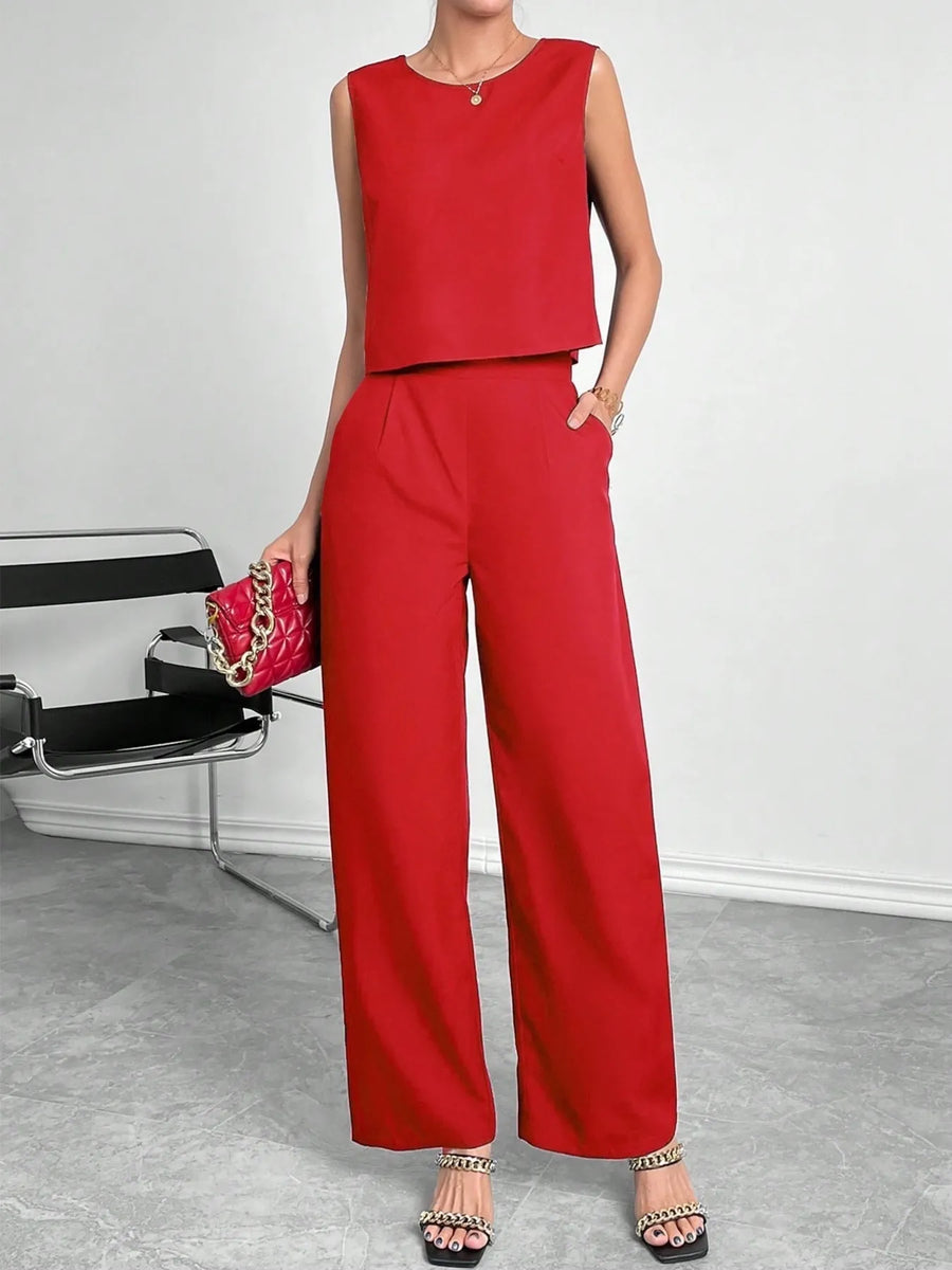 Person wearing a red outfit with wide-leg pants and a matching top, standing next to a chair.