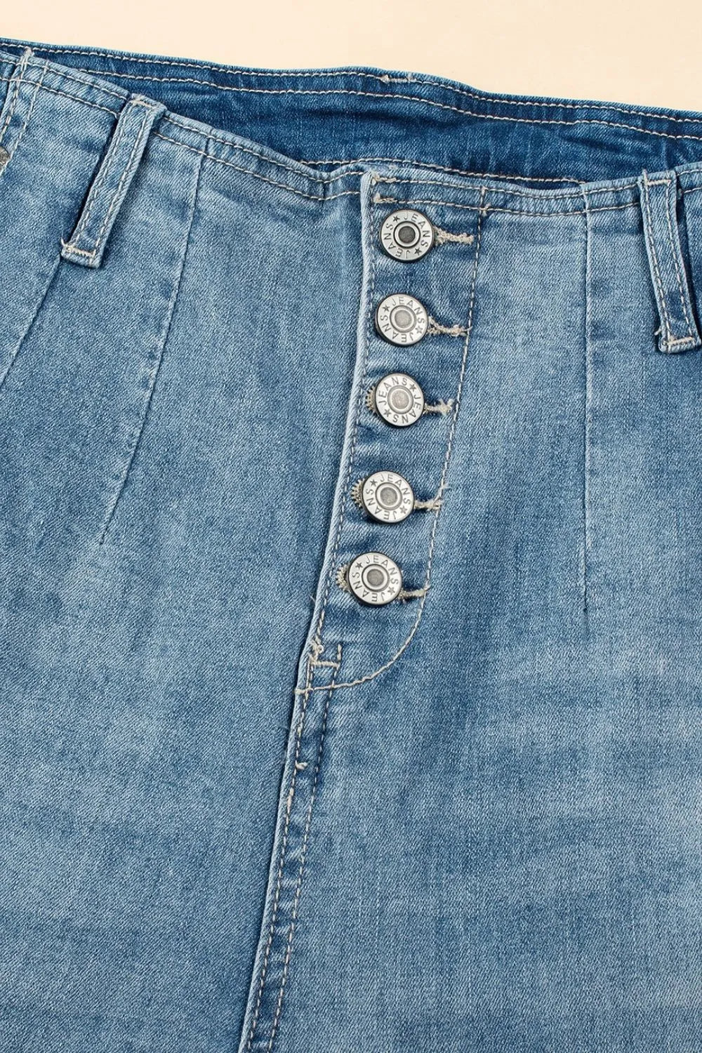 Close-up of blue denim jeans with button details on a beige background