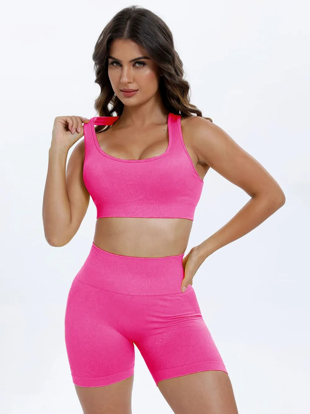Woman wearing a pink sports bra and shorts set on a light gray background