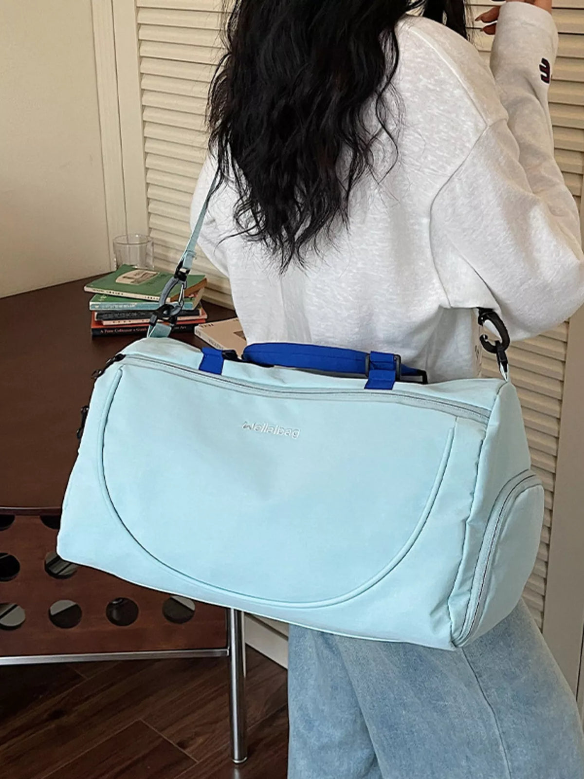 Person holding a light blue bag with a blue strap indoors.