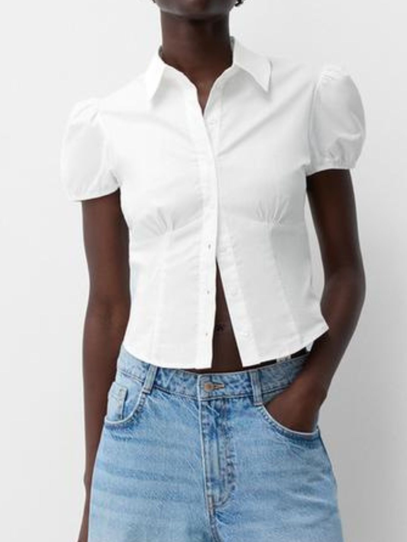 Person wearing a white short-sleeve blouse and blue jeans on a plain background