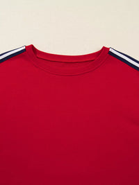 Red sweatshirt with white and navy stripes on shoulders against a beige background