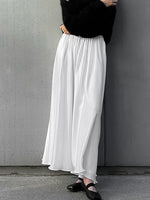Person wearing a black top and white wide-leg pants against a gray wall.