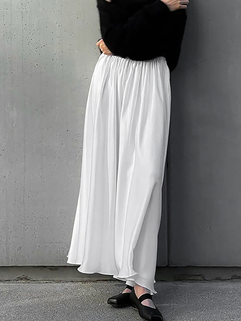 Person wearing a black top and white wide-leg pants against a gray wall.