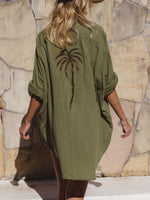 Person wearing a green dress with a palm tree design against a stone wall.