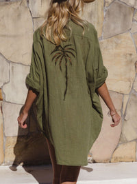 Person wearing a green dress with a palm tree design against a stone wall.