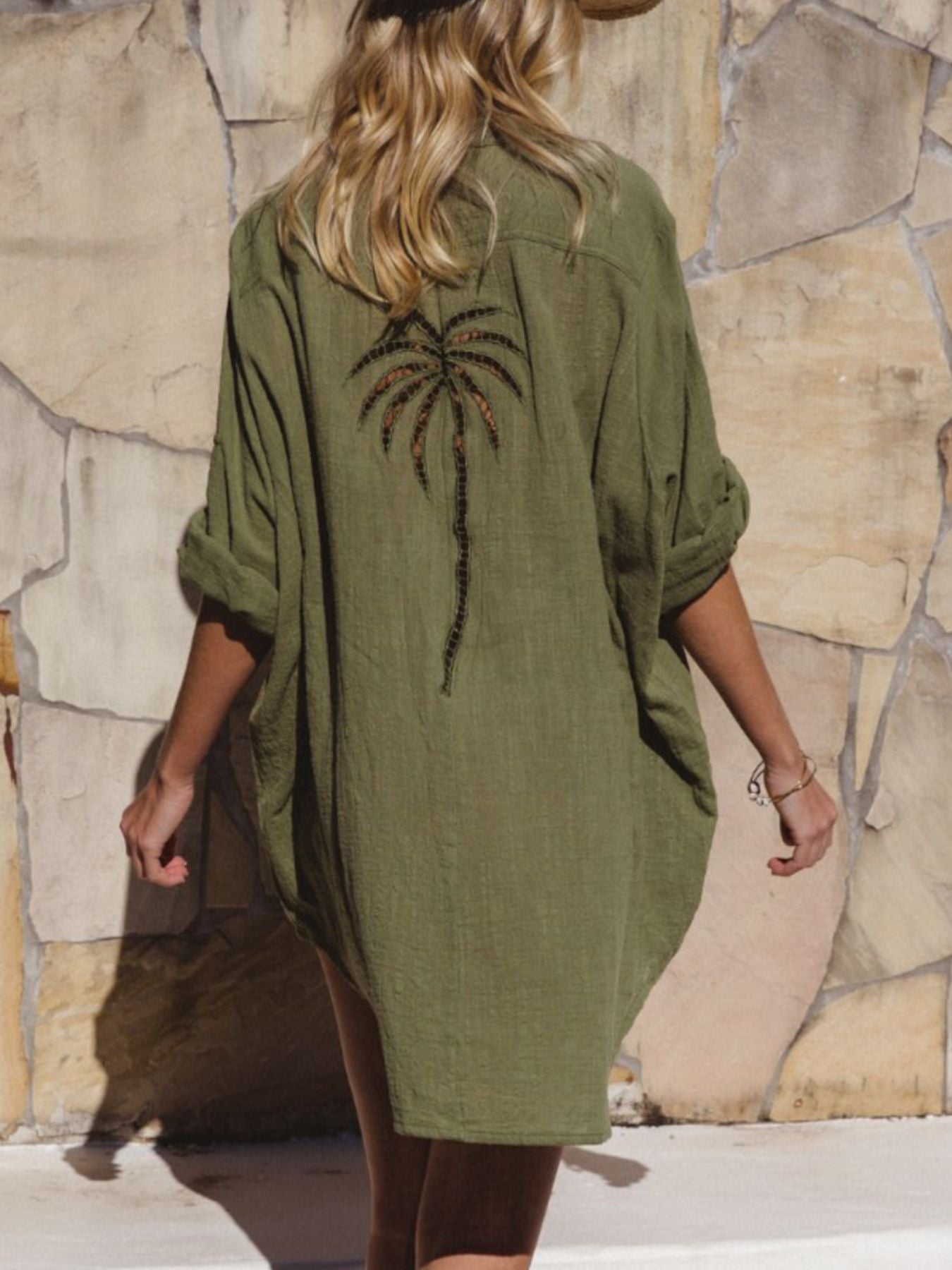 Person wearing a green dress with a palm tree design against a stone wall.