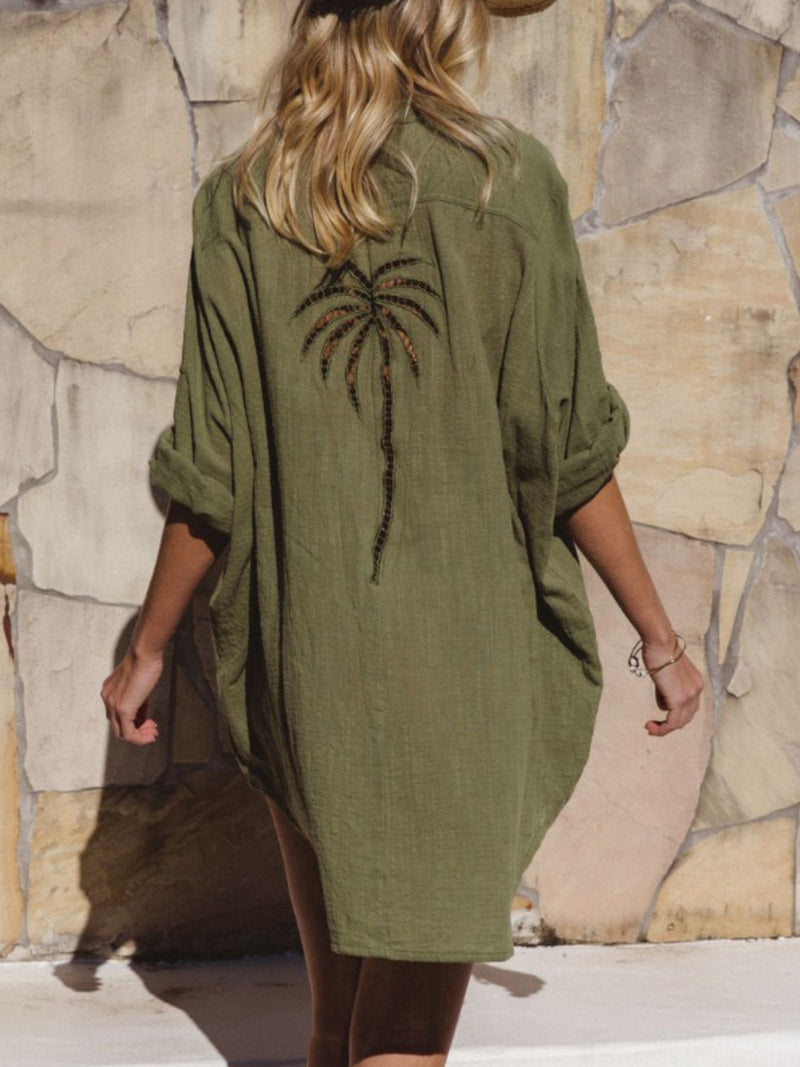 Person wearing a green dress with a palm tree design against a stone wall.