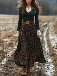 Woman in a green top and plaid skirt standing in a field with mountains in the background
