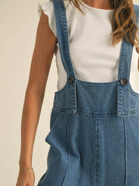Person wearing blue denim overalls on a plain background