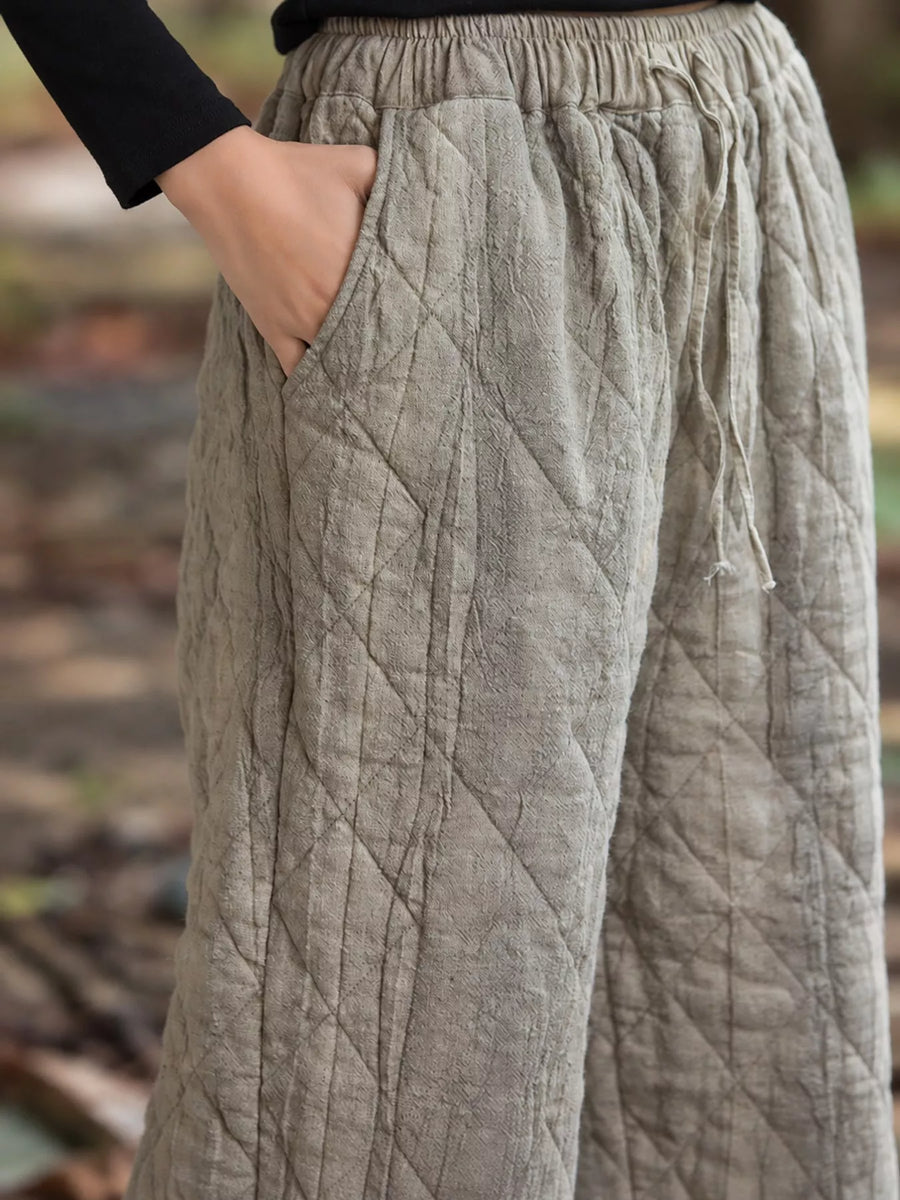 Close-up of a person wearing quilted wide-leg pants in a light taupe-gray color, with a hand in the side pocket and a black long-sleeve top visible.