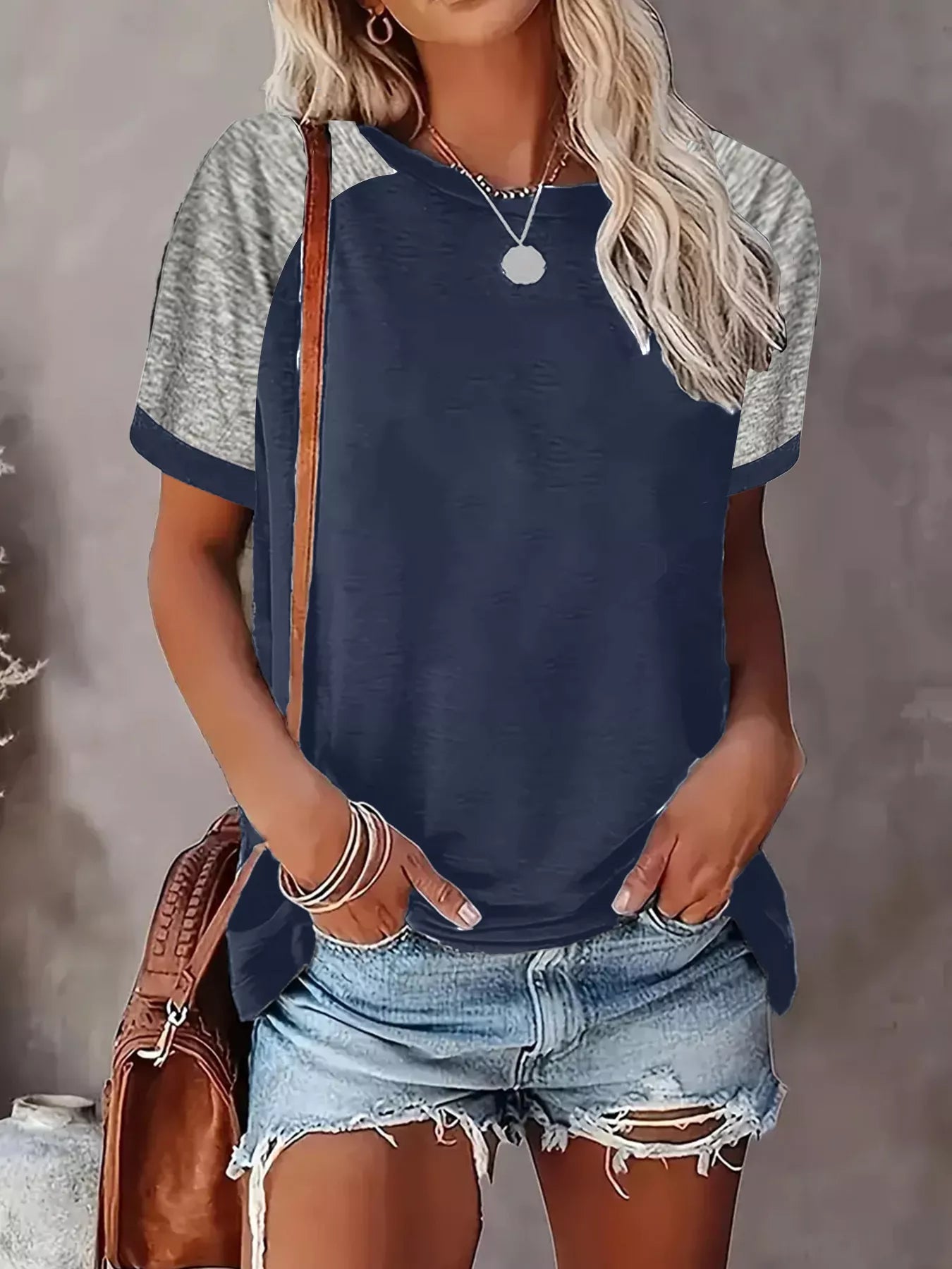 Woman wearing a navy blue and gray raglan sleeve shirt with denim shorts against a gray background.