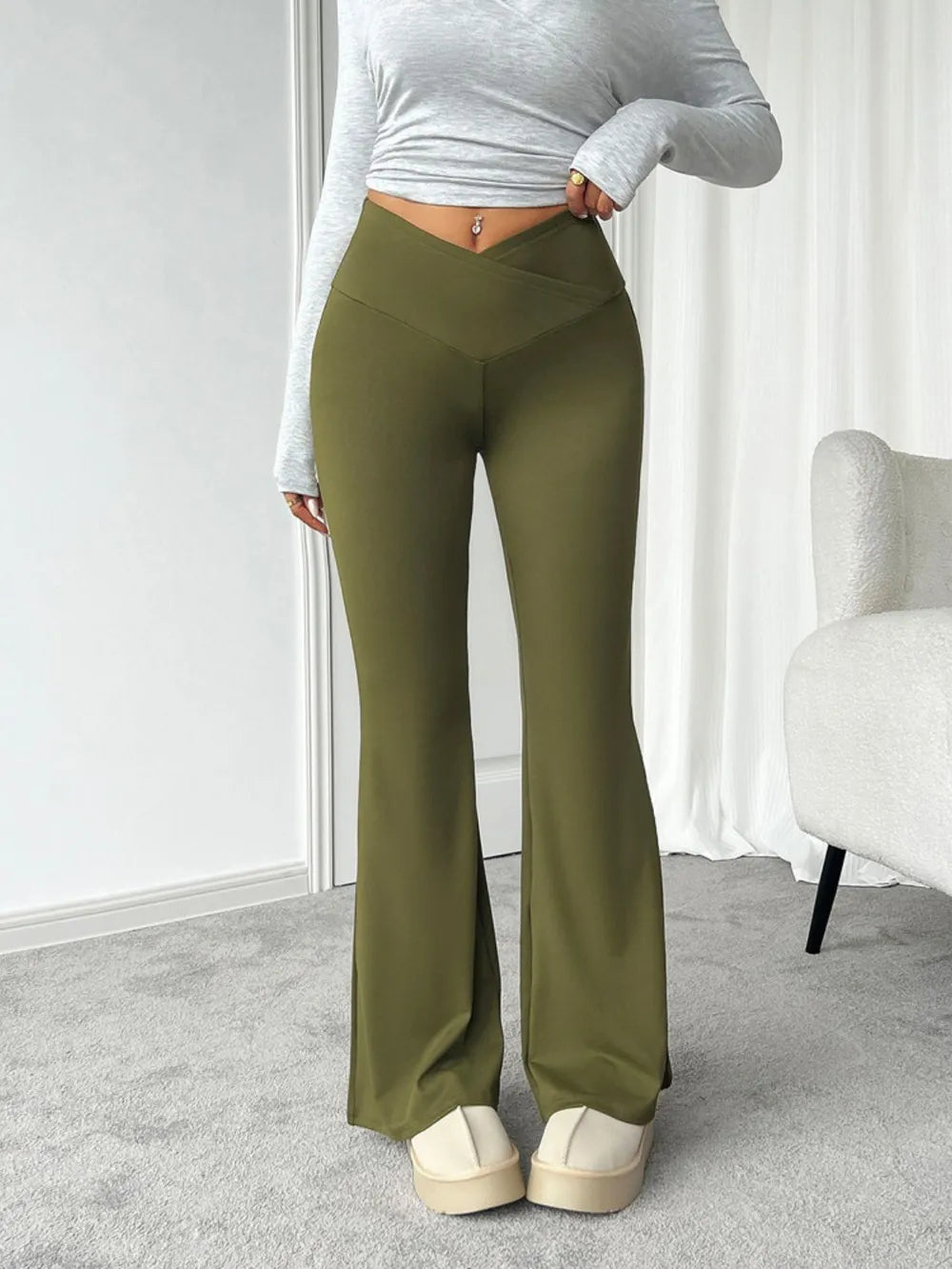 Person wearing olive green flared pants and a gray long-sleeve top in a minimalistic room.