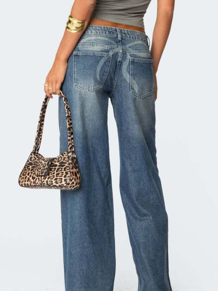 Person wearing blue jeans holding a leopard print handbag on a plain background