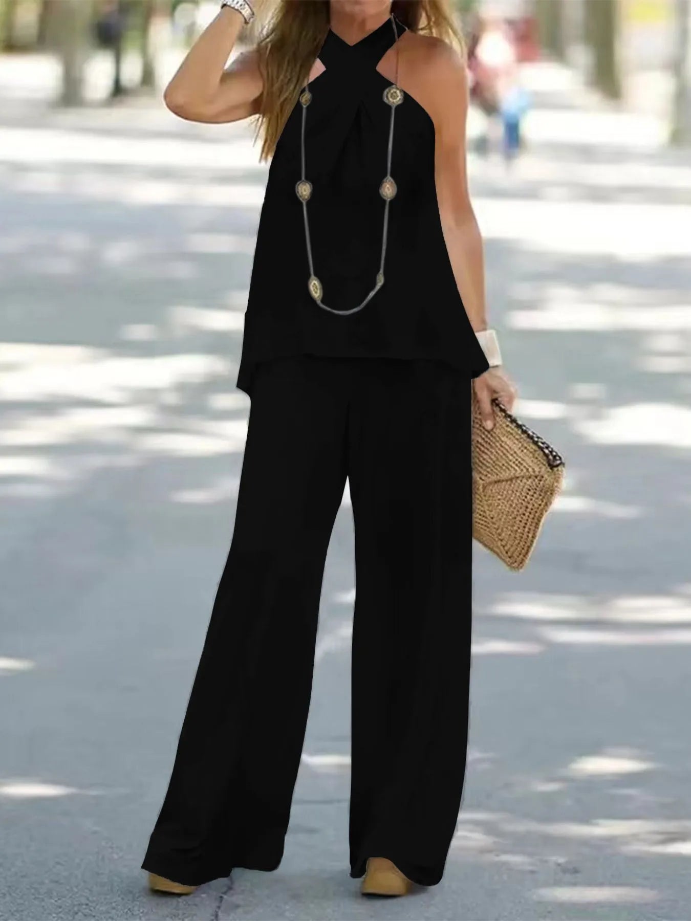 Woman wearing a black outfit with wide-leg pants and a necklace, standing on a street.