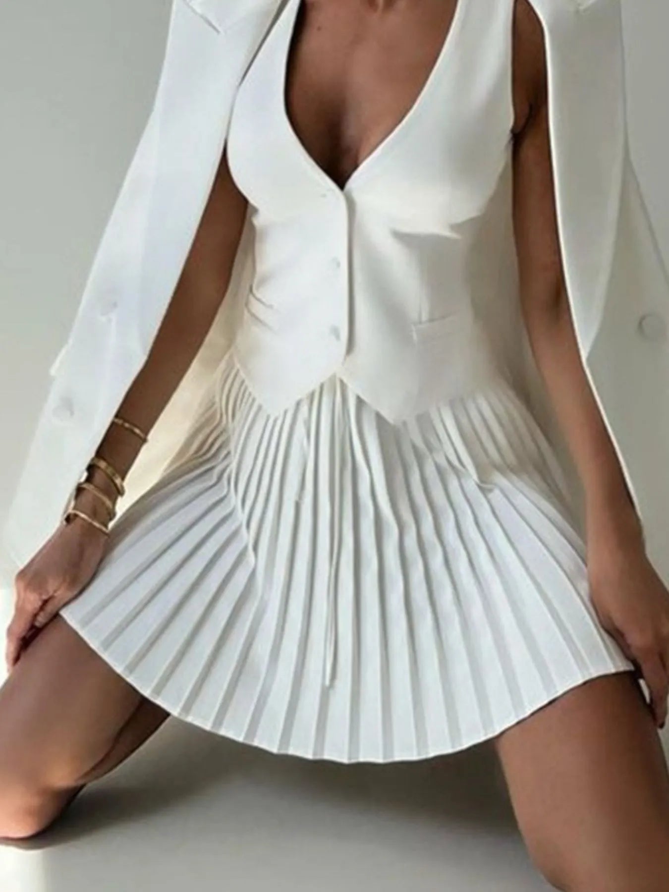 Person wearing a white pleated dress with a plain background