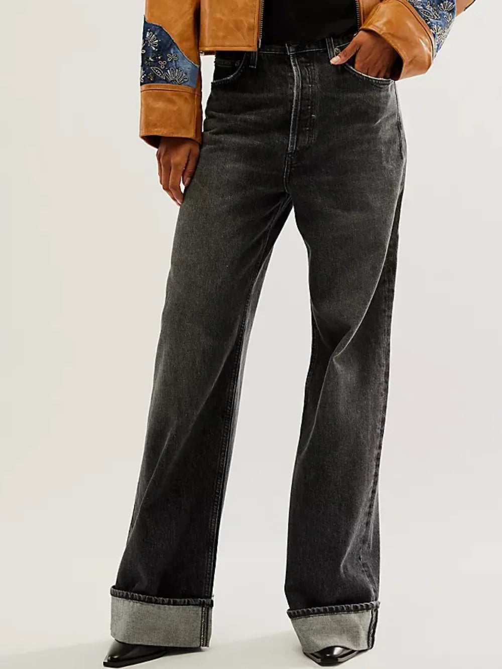 Person wearing black wide-leg jeans with a brown jacket on a white background
