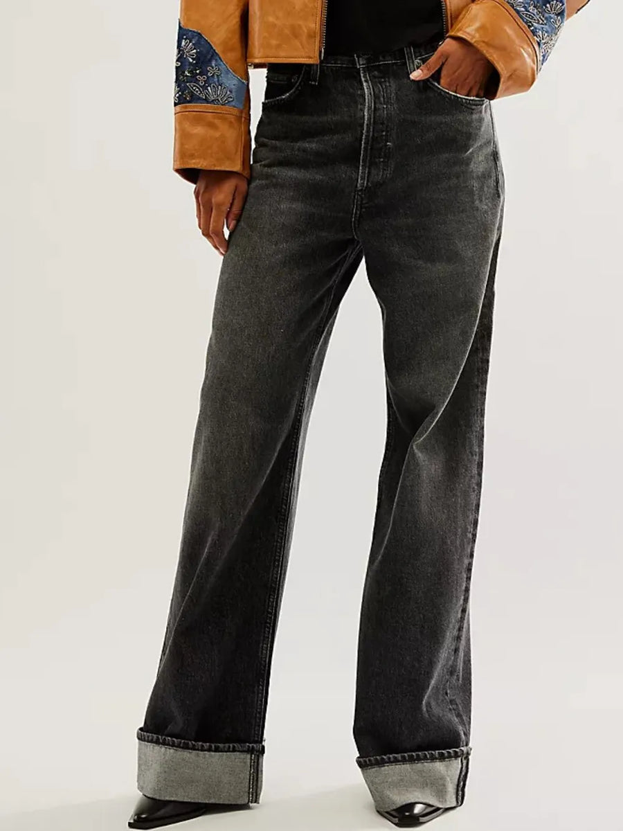 Person wearing black wide-leg jeans with a brown jacket on a white background
