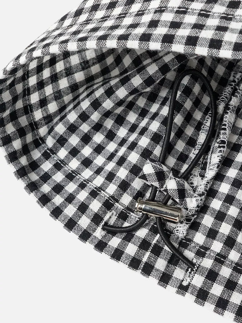 Close-up of a black and white gingham checkered fabric product with a black drawstring and silver metal toggle, photographed on a light gray background.