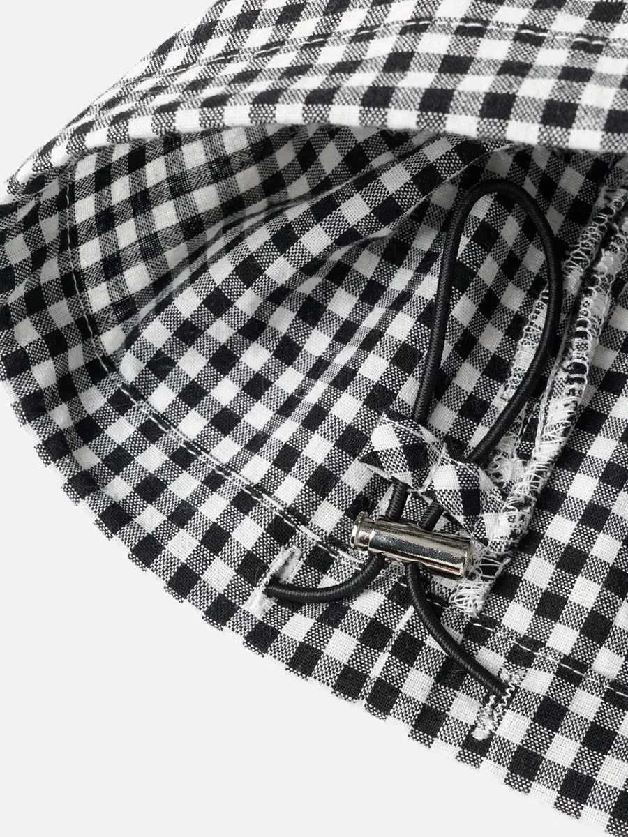 Close-up of a black and white gingham checkered fabric product with a black drawstring and silver metal toggle, photographed on a light gray background.