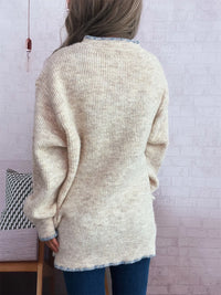 Person wearing a beige cardigan in a room with a white brick wall.