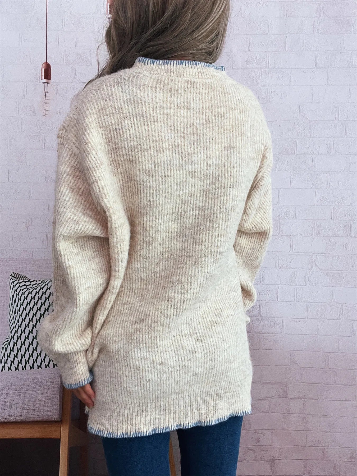 Person wearing a beige cardigan in a room with a white brick wall.