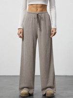 Person wearing brown wide-leg pants with a white top on a plain background