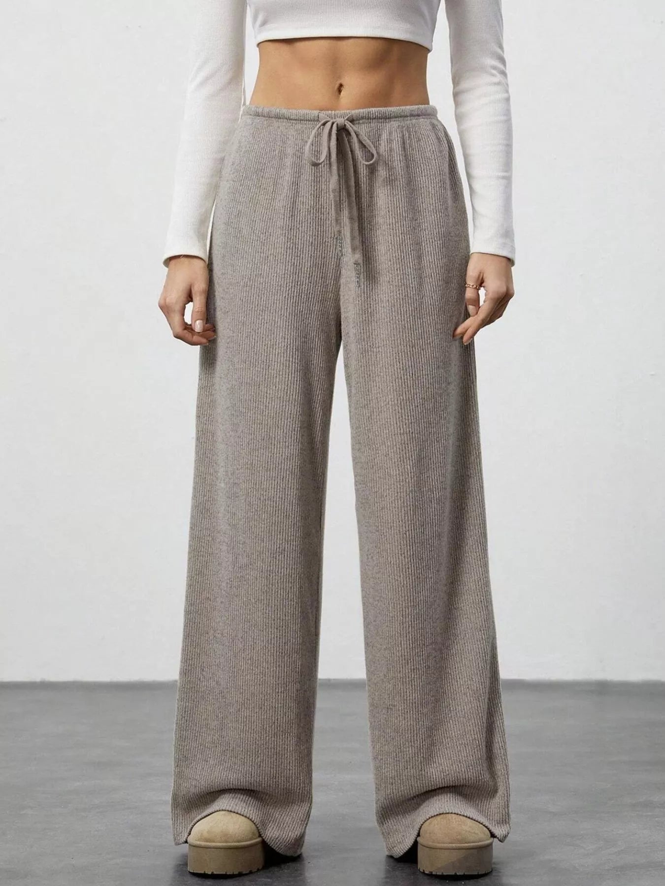 Person wearing brown wide-leg pants with a white top on a plain background