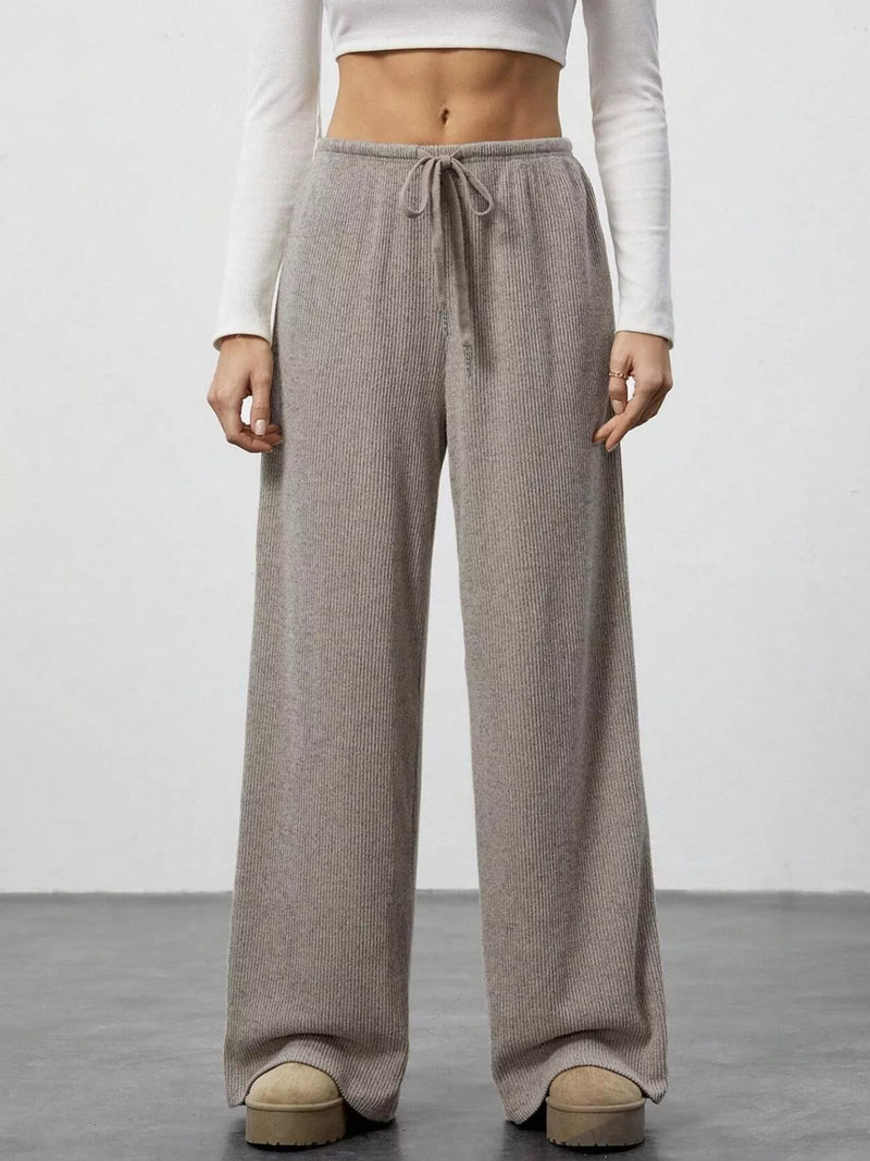 Person wearing brown wide-leg pants with a white top on a plain background
