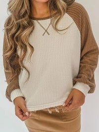 Person wearing a beige and brown sweater with a plain background