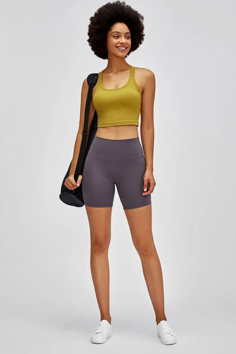 Woman wearing a yellow tank top and purple shorts with a black bag on a white background