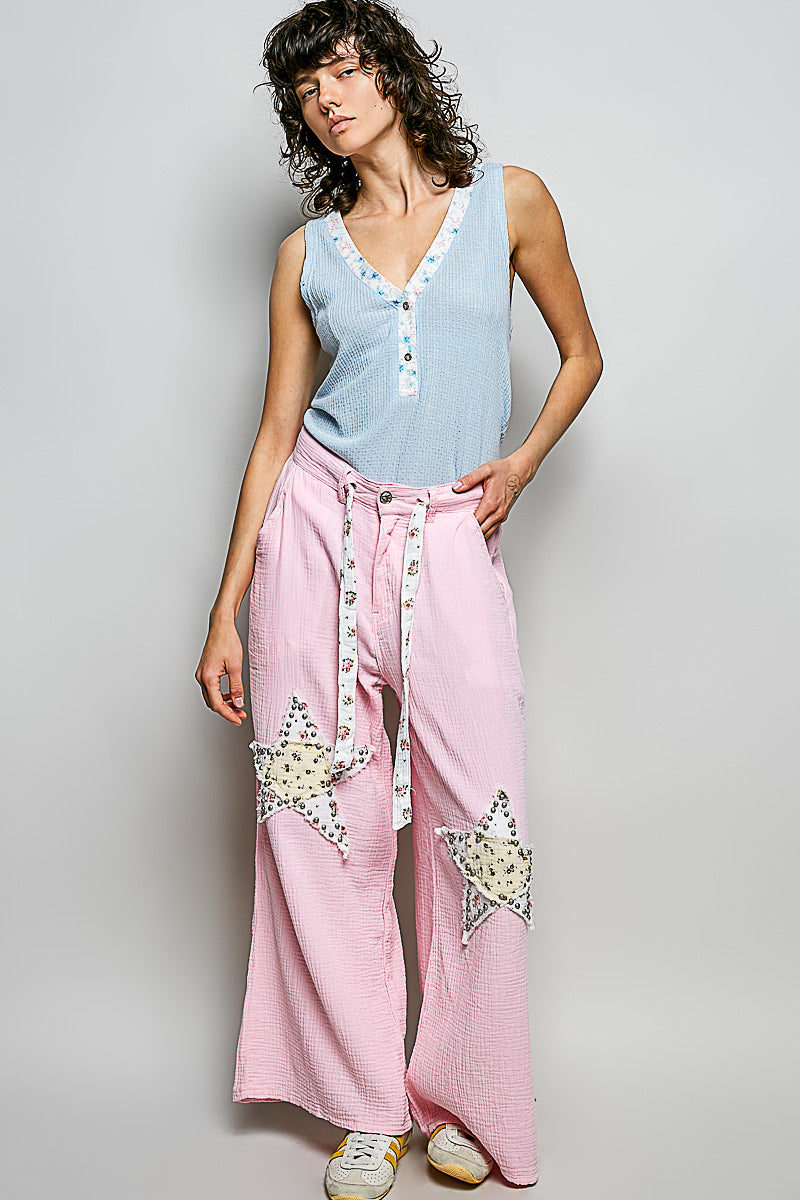 Woman wearing a light blue sleeveless top and pink pants with star designs on a plain background