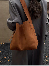 Brown leather shoulder bag worn by a person with a neutral background