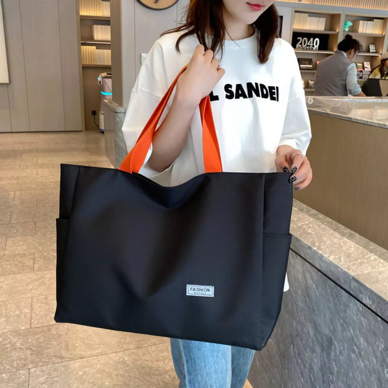 Person holding a black tote bag with an orange strap in a store setting