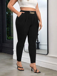 Person wearing black pants with a gold belt standing indoors.