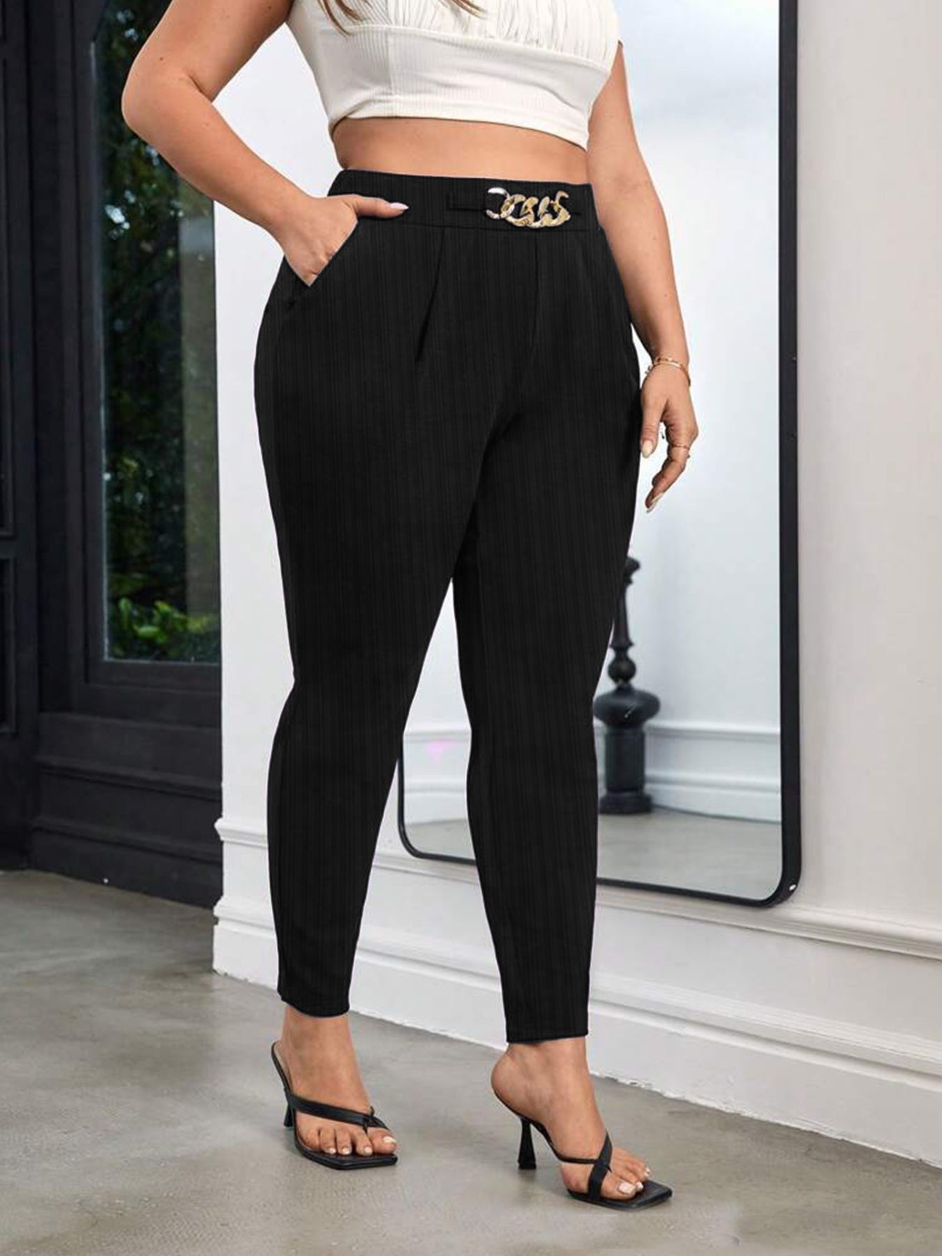 Person wearing black pants with a gold belt standing indoors.