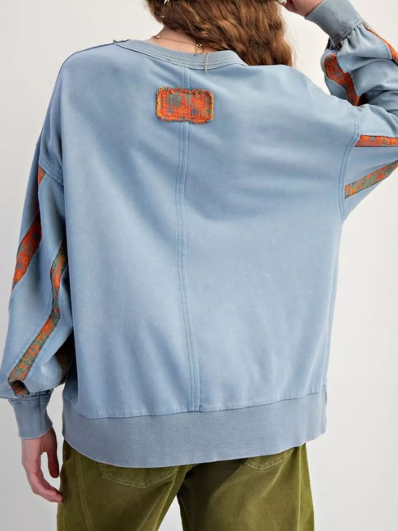 Light blue sweatshirt with orange patterns on sleeves and back, worn by a person.