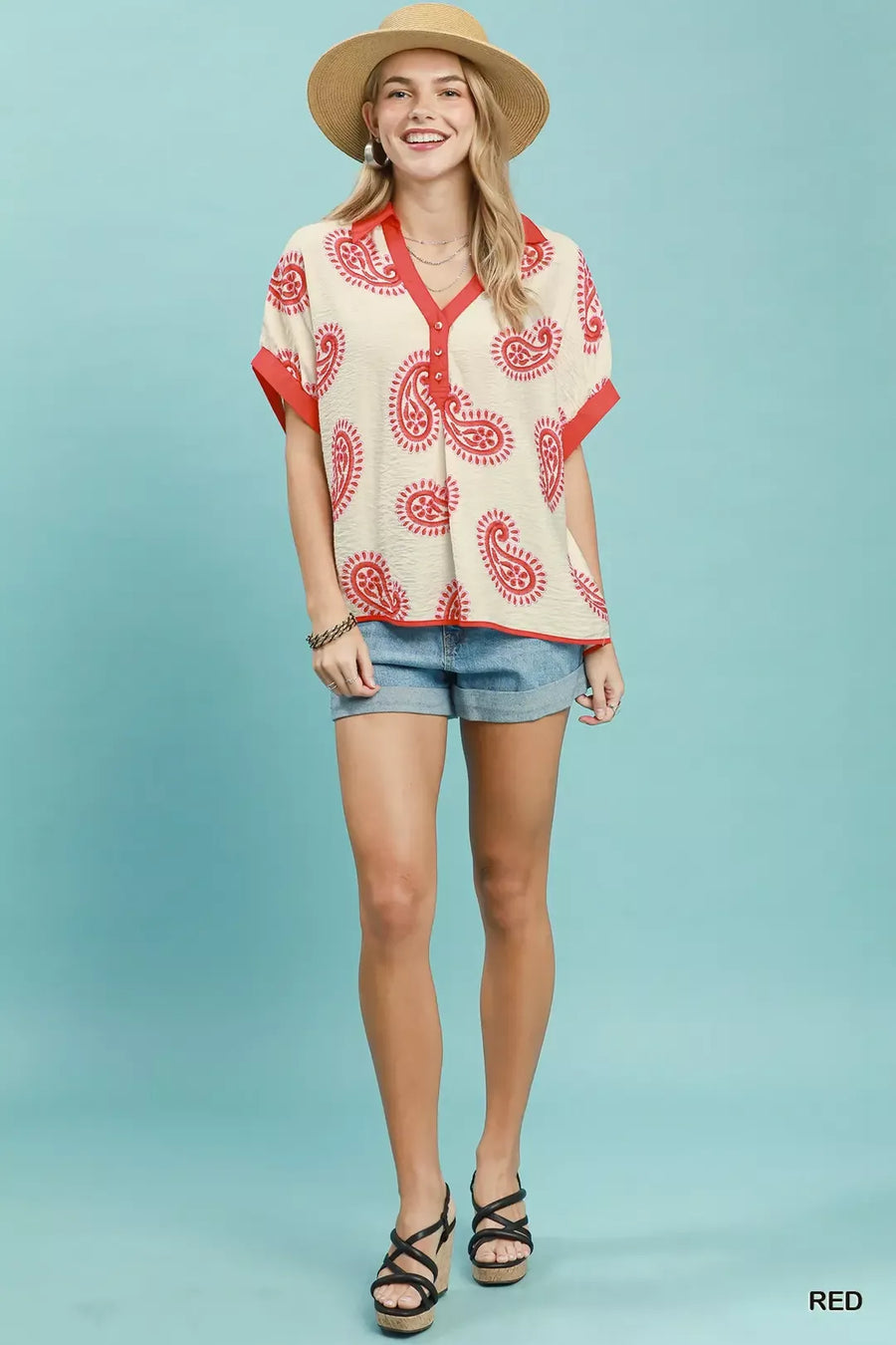 Woman wearing a red and white patterned shirt with denim shorts on a light blue background
